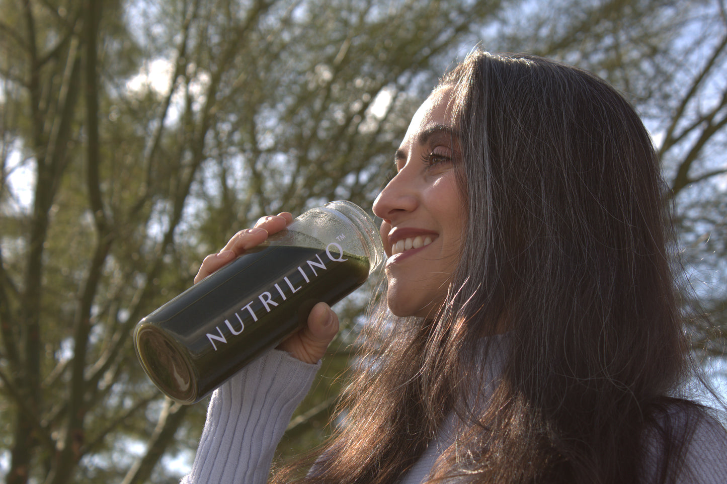 A woman drinking Nutrilinq Nourish Synbiotic Fiber on a sunny day.